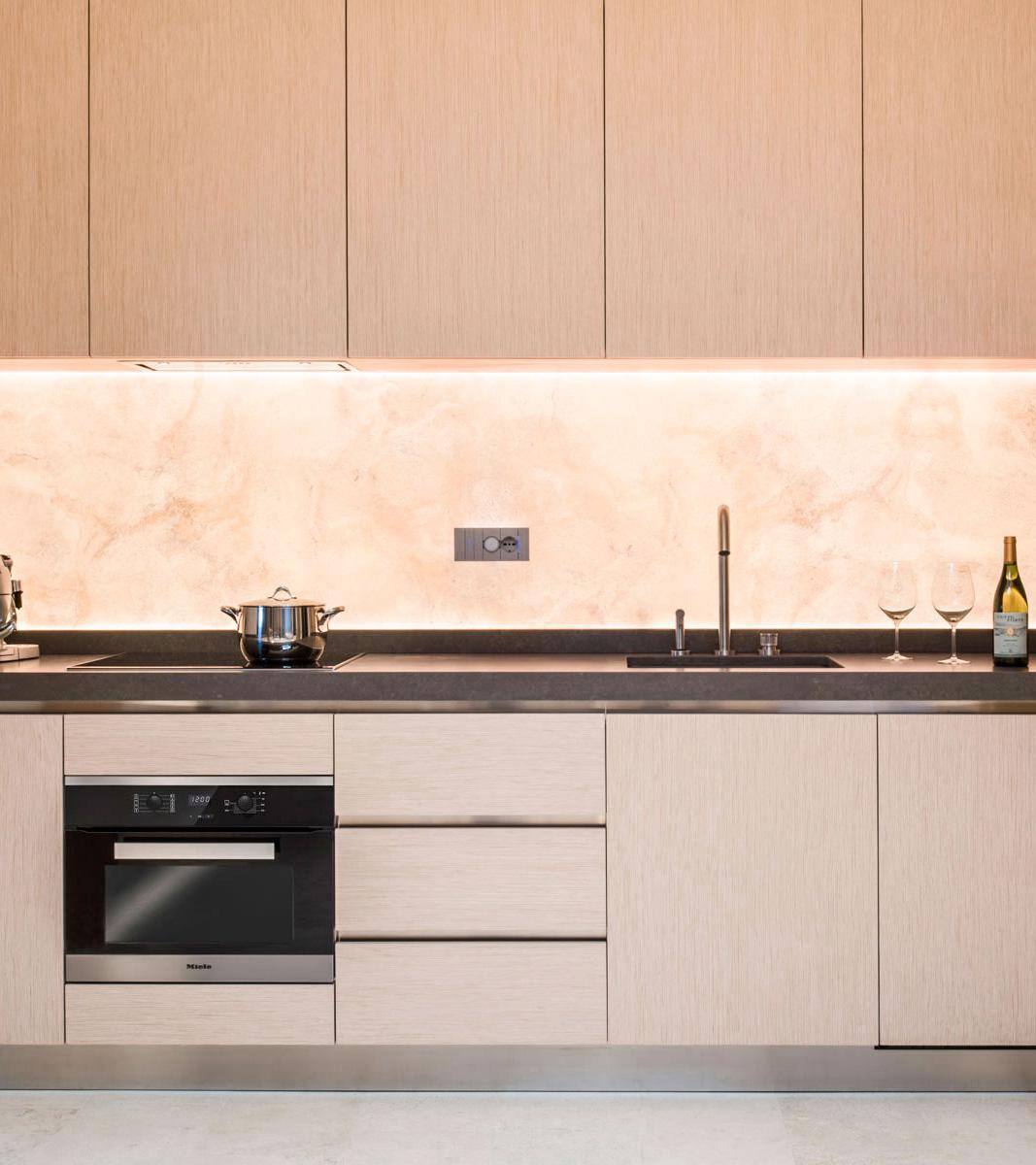Dettaglio cucina lineare moderna in legno chiaro, schienale con texture in travertino retroilluminato e top in pietra