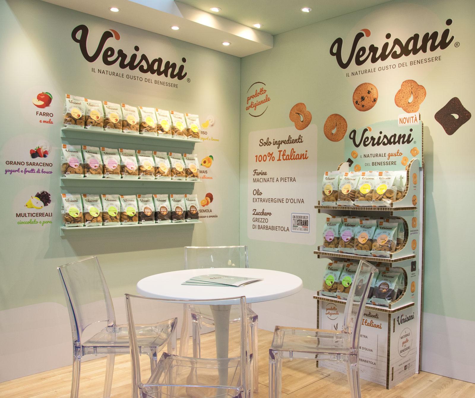 Un angolo dello stand con tavolo e sedie e un’esposizione di biscotti sulle pareti stampate con immagini e grafica