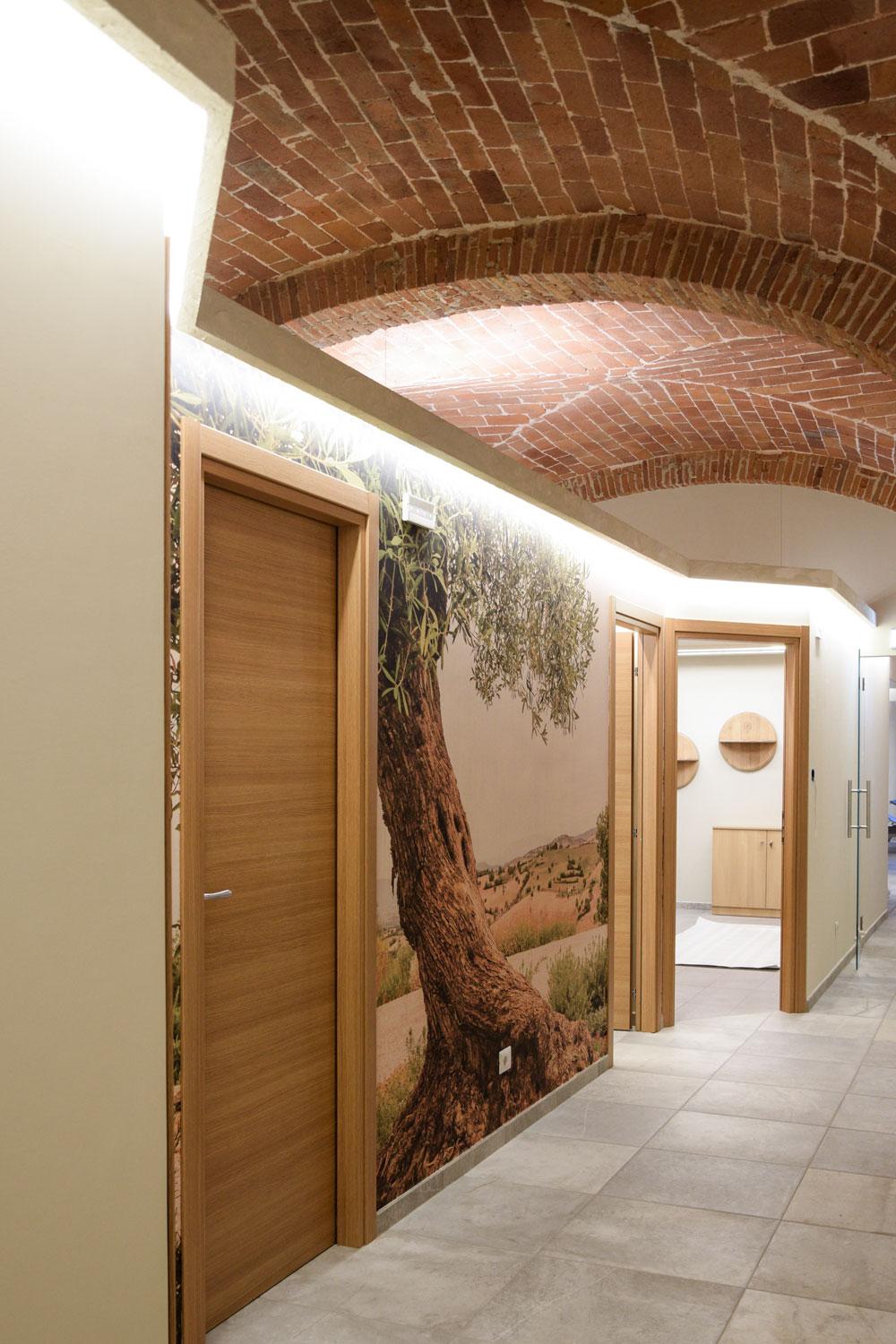 Corridoio della zona trattamenti con volte in mattoni e pareti rivestite con carta da parati a tema campagna toscana