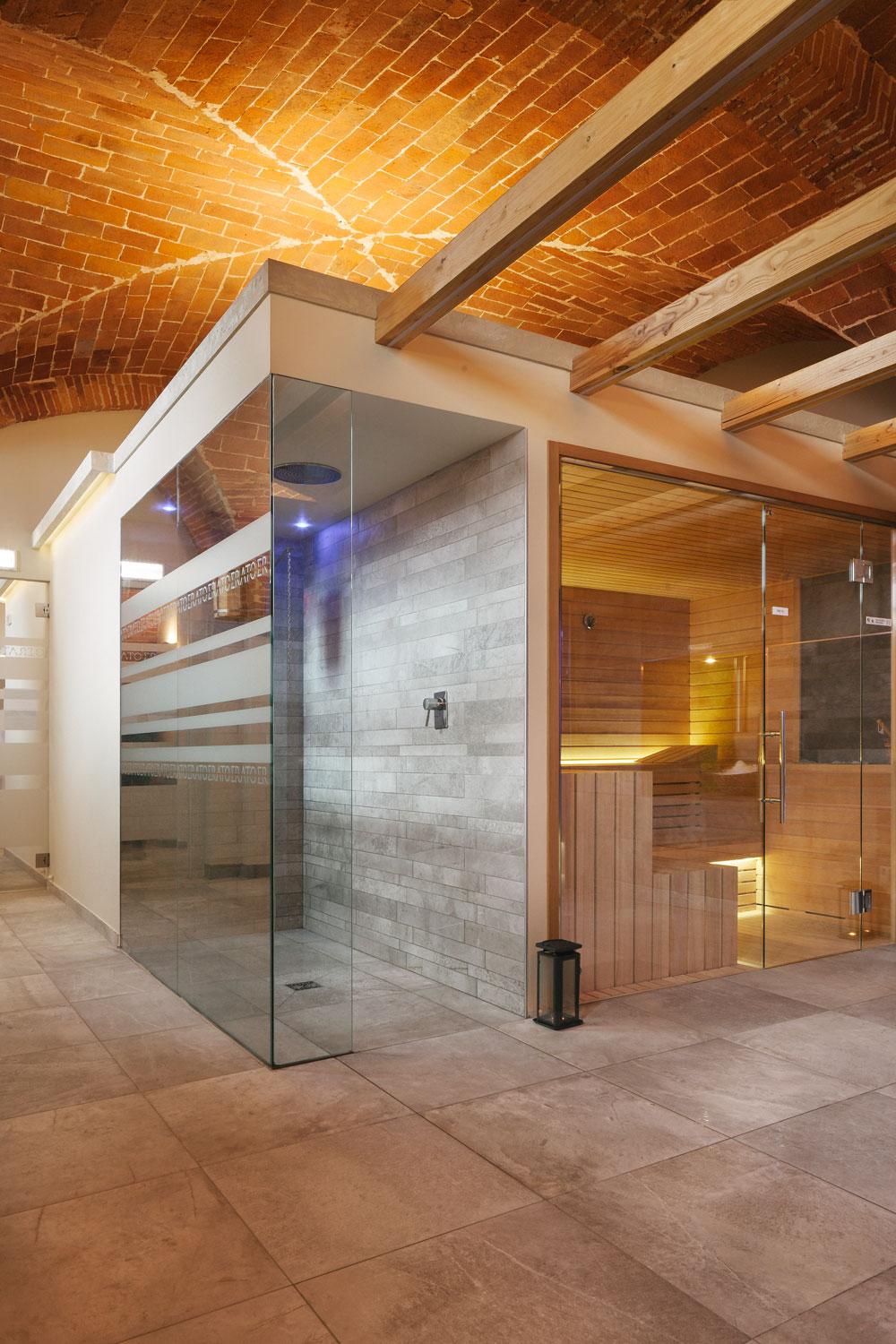 Sauna con porta a vetri e doccia con secchiello in legno