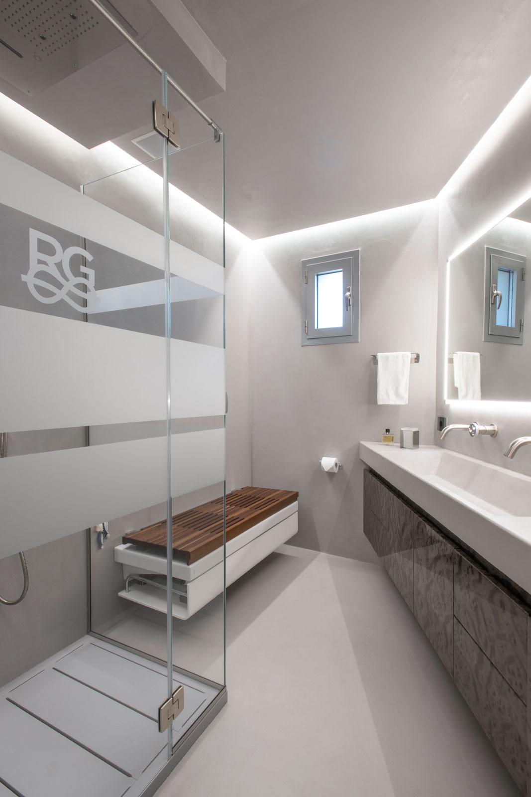 Bagno moderno in resina di cemento con doccia wellness, box in cristallo e panca con sanitari integrati