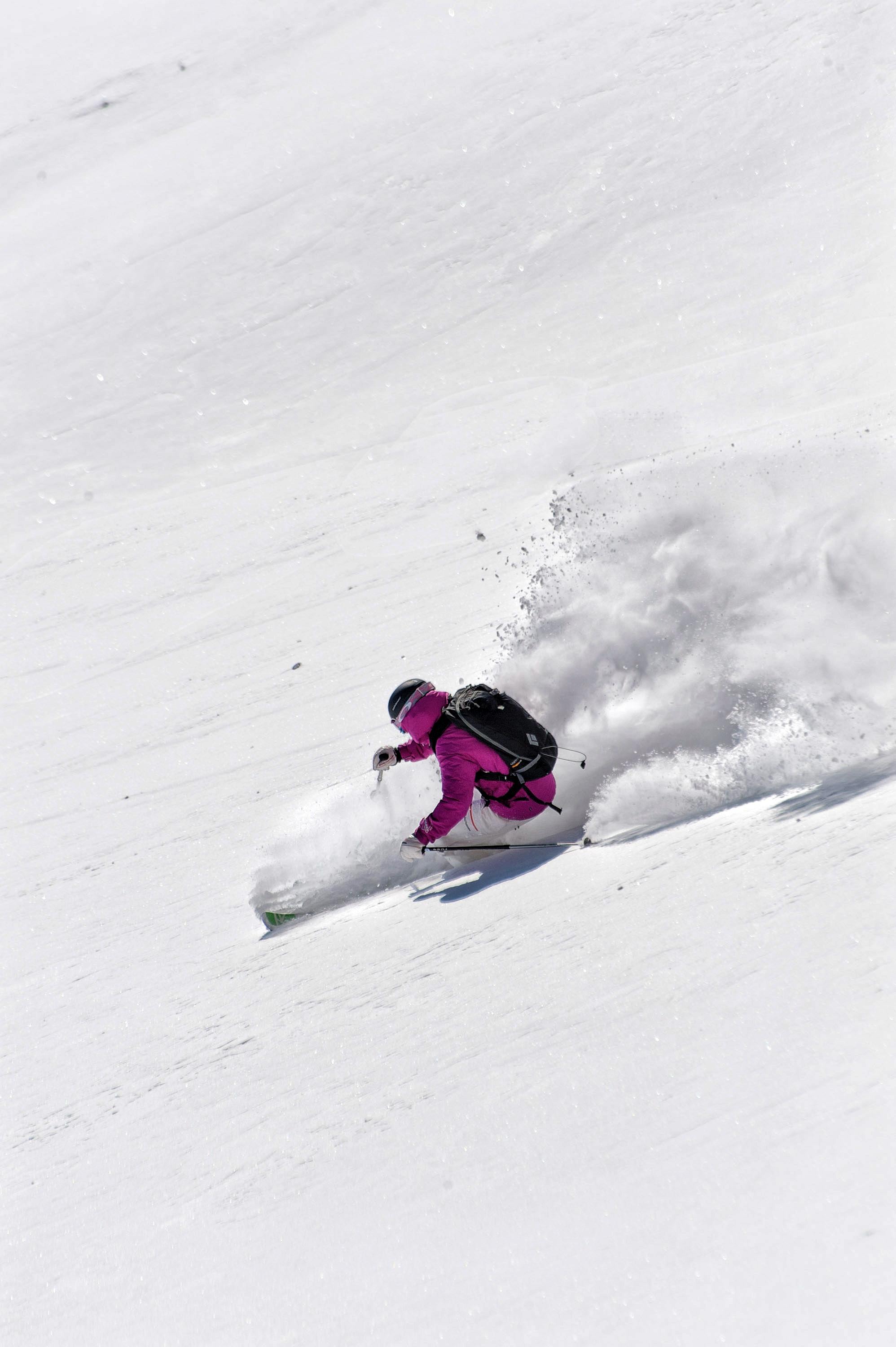 sciatore in neve fresca con giacca viola e zaino nero